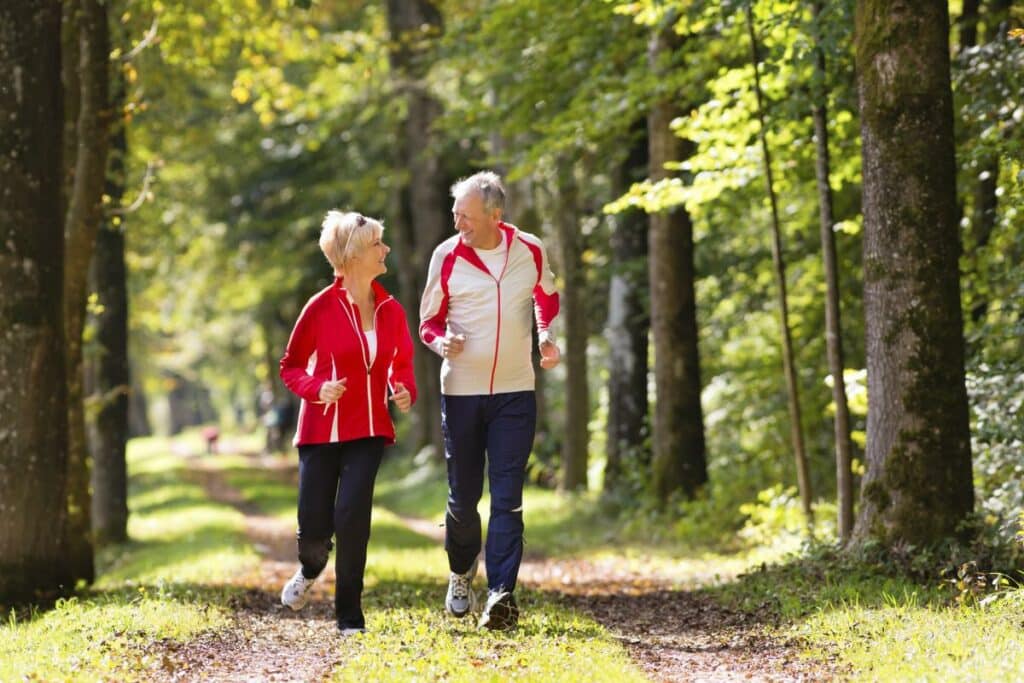 Deux personnes âgés sont entrain de courir dans les bois en souriant